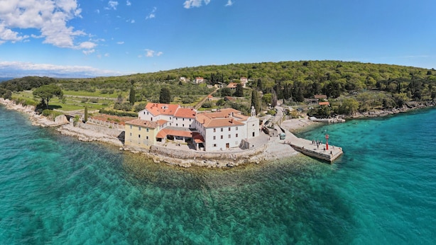 Un pueblo costero con edificios cerca del agua, un muelle y una colina al fondo.