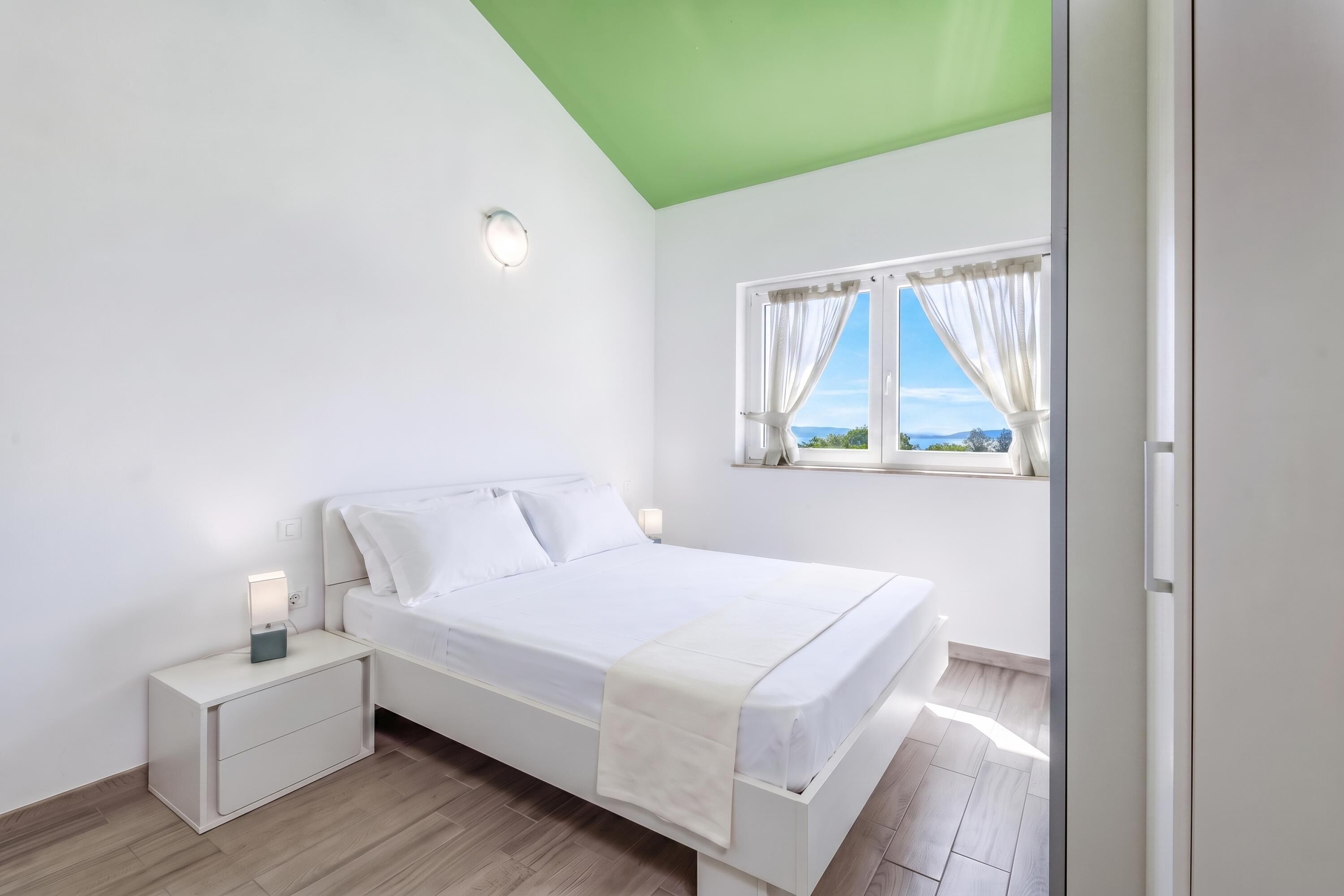 Un dormitorio con cama, mesitas de noche, una ventana con cortinas y vistas al exterior.