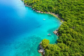 Vue aérienne d’une zone côtière caractérisée par des eaux turquoise limpides, une végétation luxuriante et des affleurements rocheux.