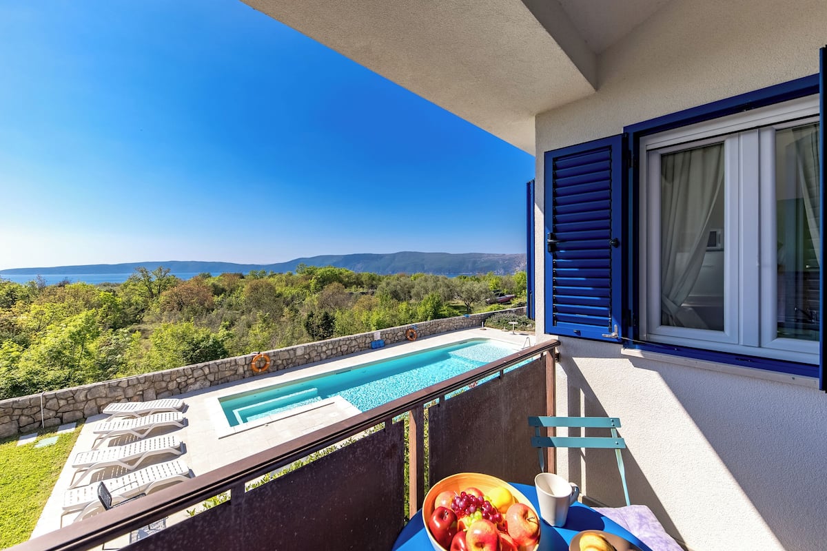 A balcony with a pool, a table with fruit, and a view of the landscape.