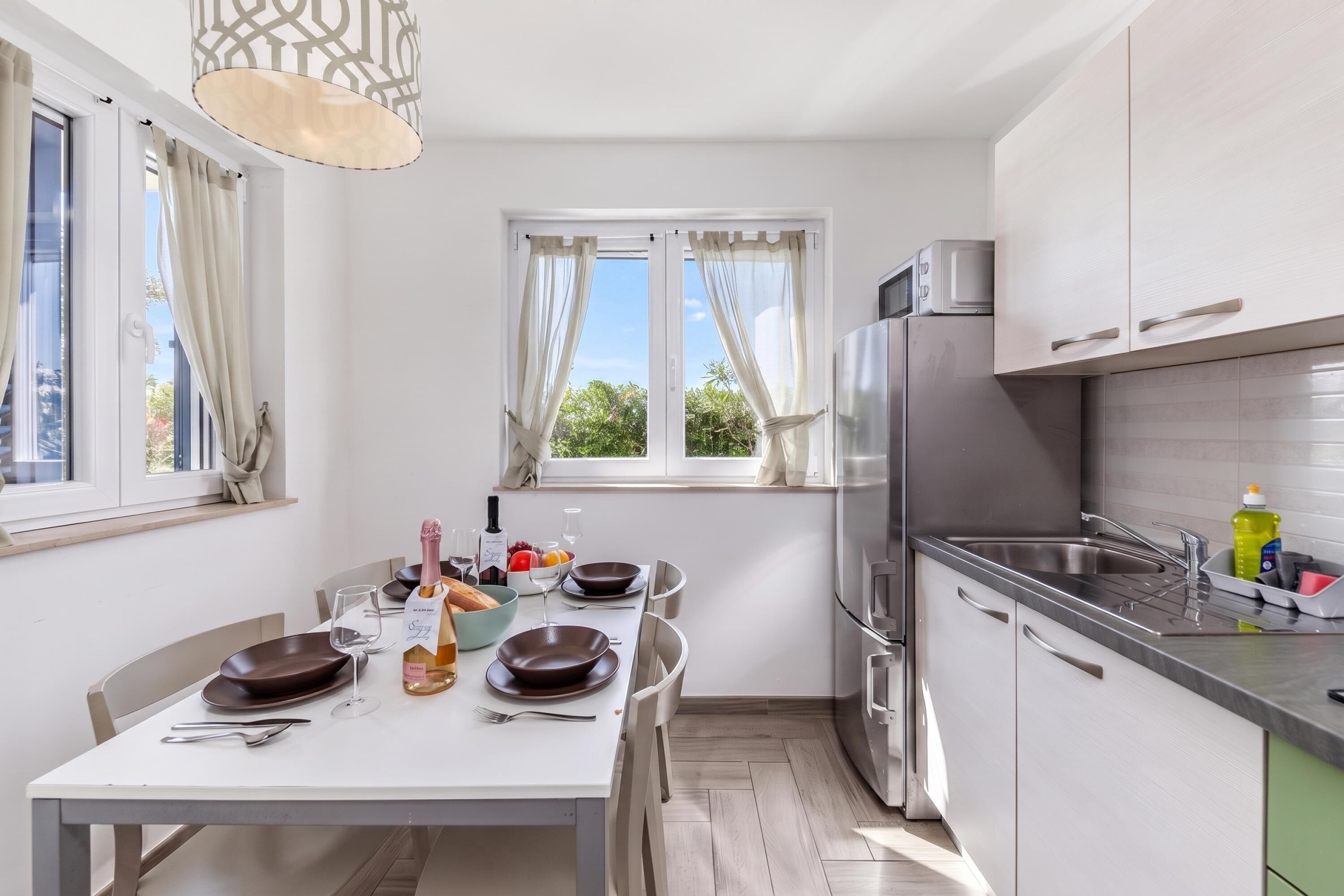 A modern kitchen with a dining area, stainless steel appliances, and a view of greenery outside.