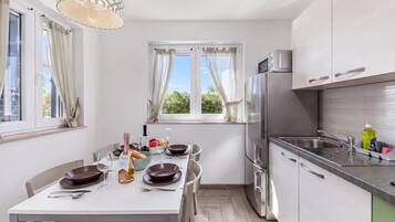 A modern kitchen with a dining area, stainless steel appliances, and a view of greenery outside.