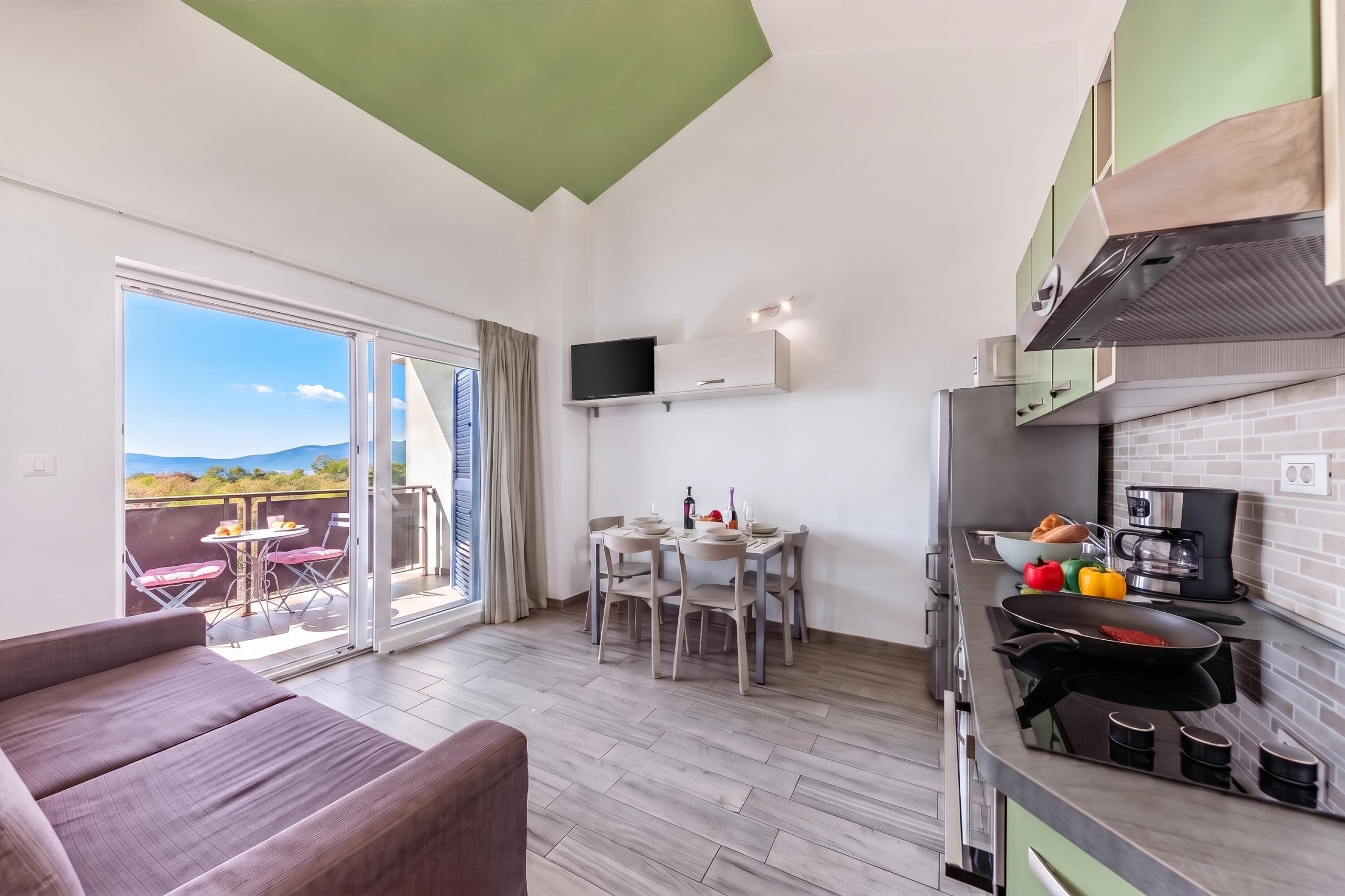 A modern kitchen with a dining area, a flat-screen TV, and a balcony with a scenic view.