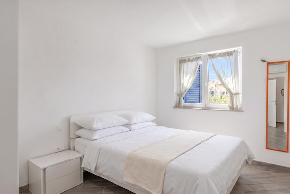 A bedroom with a bed, a bedside table, a window with curtains, and a mirror with an orange frame.