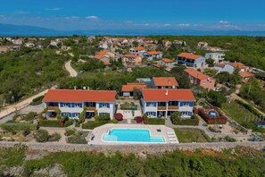 A residential area with a swimming pool, houses with red roofs, and a clear sky. - Wabi Sabi Apartments With Pool (Krk)