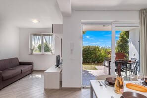 A modern living room with a sofa, a flat-screen TV, and a dining area with a table set for two. - Wabi Sabi Apartments With Pool (Krk)