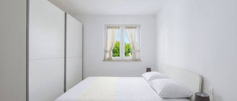 Une chambre à coucher comprenant un lit, une table de chevet, une lampe, une fenêtre avec des rideaux et une armoire.