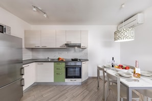 A modern kitchen with a built-in oven, a stainless steel refrigerator, and a dining area with a table set for two. - Wabi Sabi Apartments With Pool (Krk)