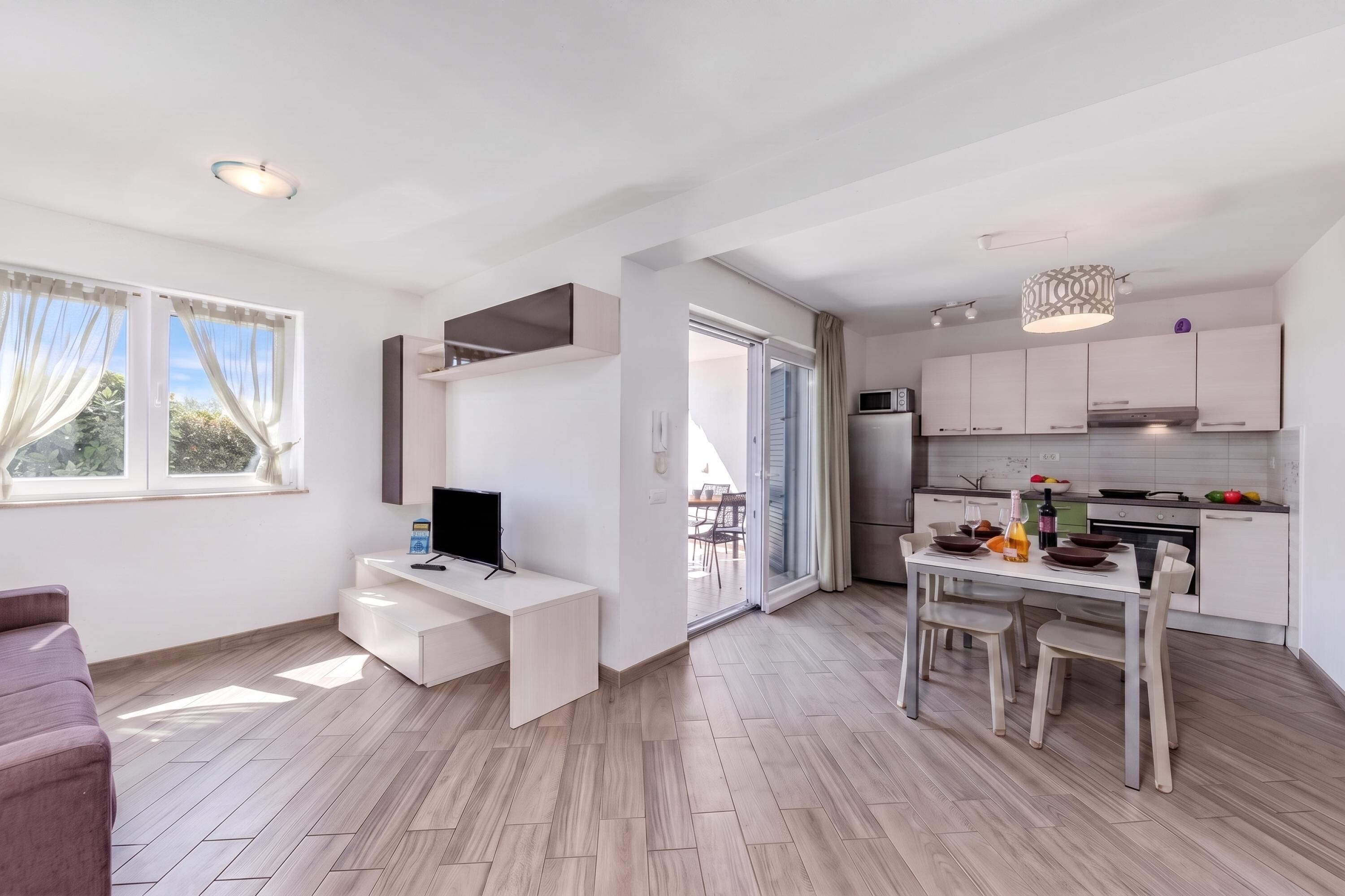A modern kitchen with white cabinets, a dining table set for four, and a TV on a white desk.
