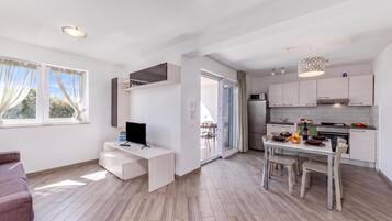 A modern kitchen with white cabinets, a dining table set for four, and a TV on a white desk.