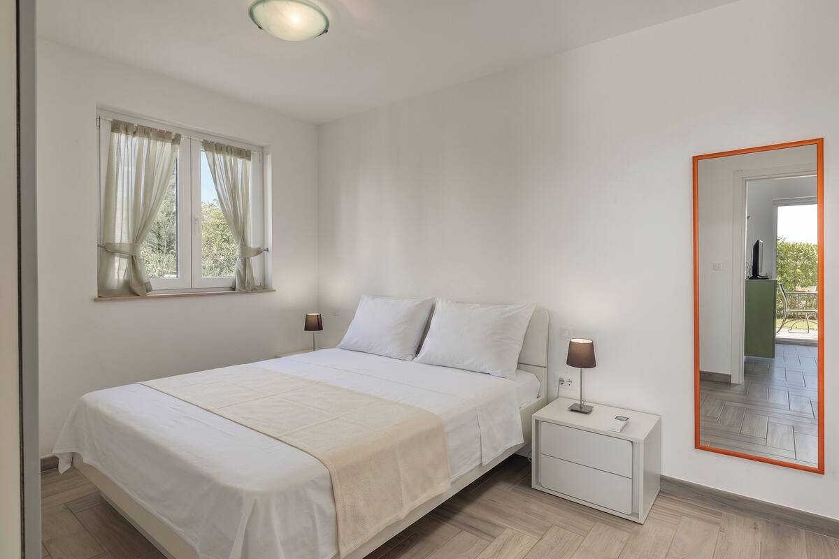 A bedroom with a bed, bedside tables, a mirror, and a window with curtains.