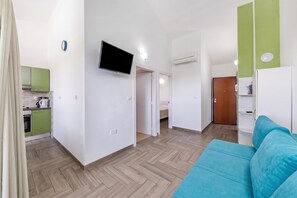 A modern apartment with a kitchenette, a flat-screen TV, a bed, and a blue sofa.