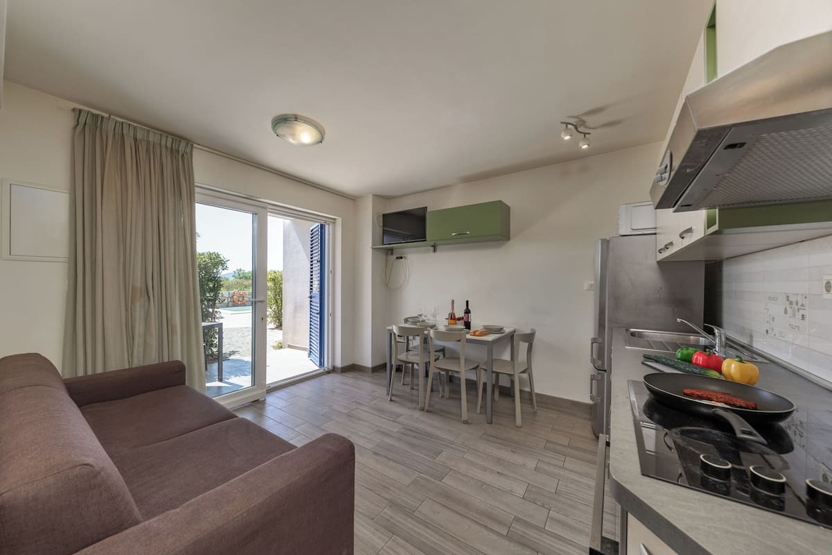 A modern kitchen with a dining area, a sofa, and a sliding glass door to the outside.