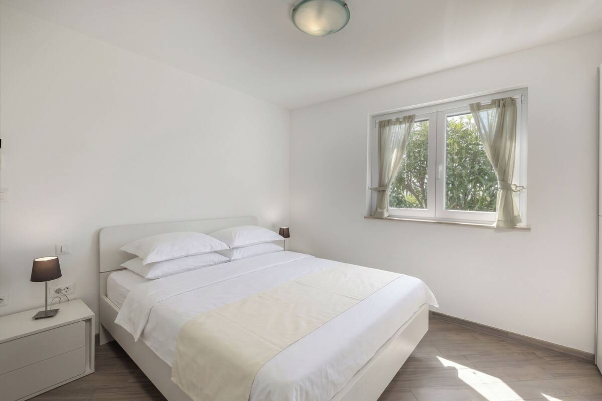 A bedroom with a bed, bedside table, lamp, and window with curtains.