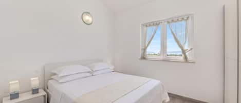 Un dormitorio con cama, mesitas de noche, una ventana con cortinas e iluminación en la pared.