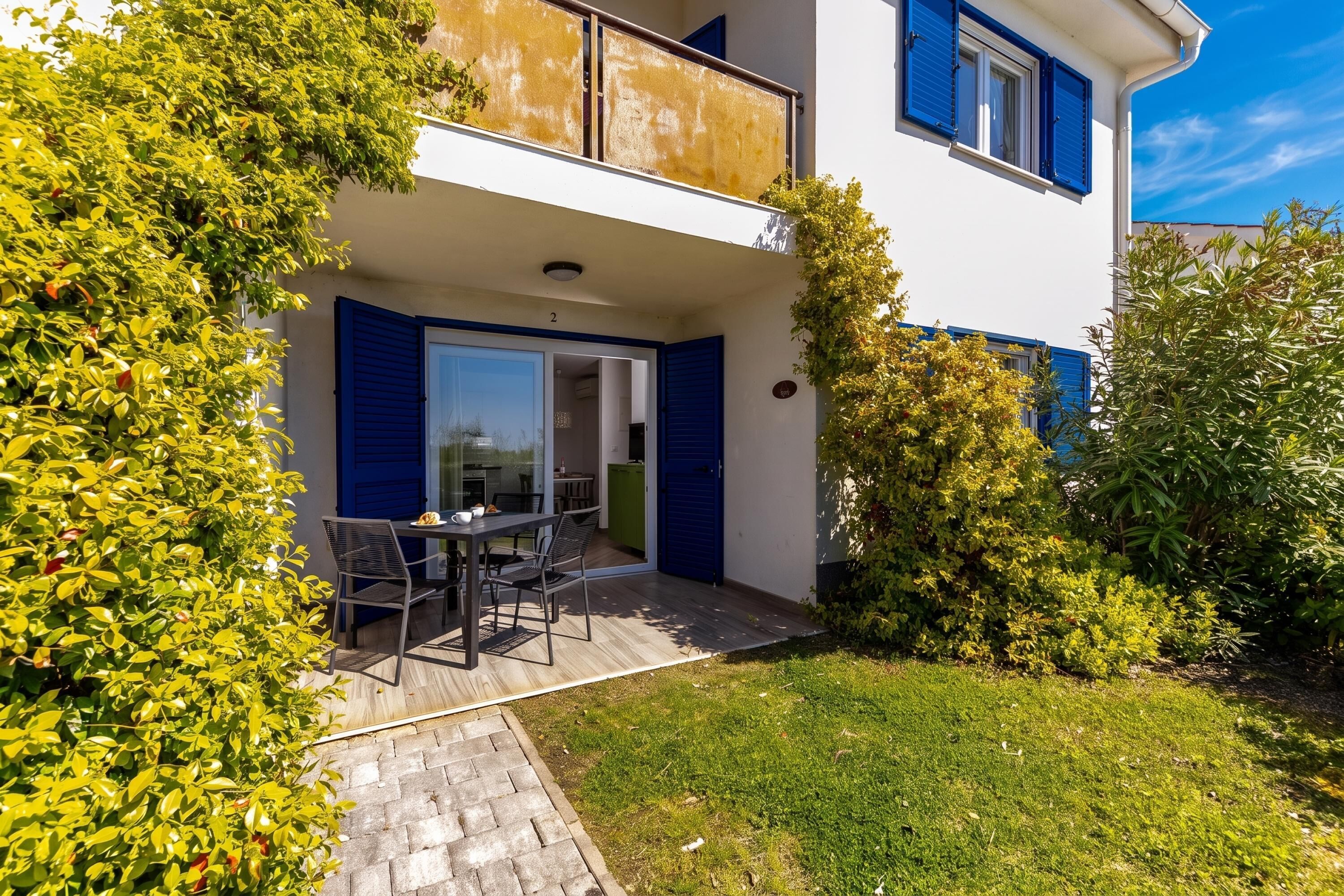 Ein zweistöckiges Gebäude mit einem Balkon, einem Essbereich mit Stühlen und einem Tisch sowie einem gepflegten Garten.