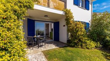 Ein zweistöckiges Gebäude mit einem Balkon, einem Essbereich mit Stühlen und einem Tisch sowie einem gepflegten Garten.