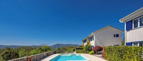Una piscina con sillones de descanso, un muro de piedra y vistas a montañas.