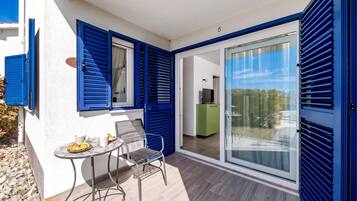 A balcony with a table, chairs, and a view of a green cabinet and a TV in the background.