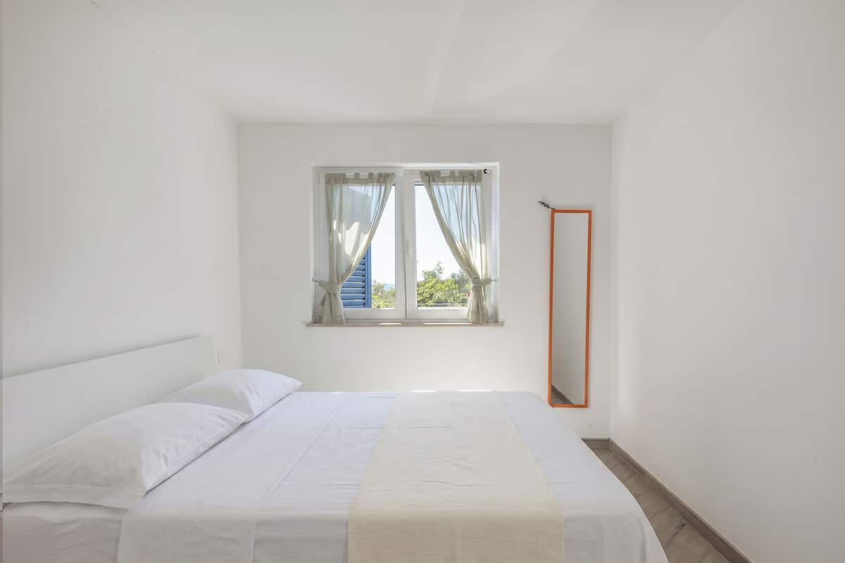 A bedroom with a bed, a window with curtains, a mirror, and a door.