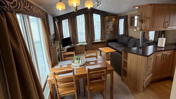 A compact RV interior with a dining area, kitchenette, and seating space. - Cabin Caravan Sleeps 6 With Parking (Abergele)