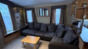 A living area with a sofa, a small wooden table, and a kitchen counter. - Cabin Caravan Sleeps 6 With Parking (Abergele)