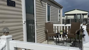 A mobile home with a balcony, two wicker chairs, a small table, and a potted plant. - Cabin Caravan Sleeps 6 With Parking (Abergele)