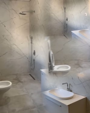 A bathroom with marble walls, a toilet, a sink, and a shower.