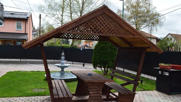 Un kiosque en bois avec une table et des bancs, entouré d’une zone pavée agrémentée d’une fontaine.