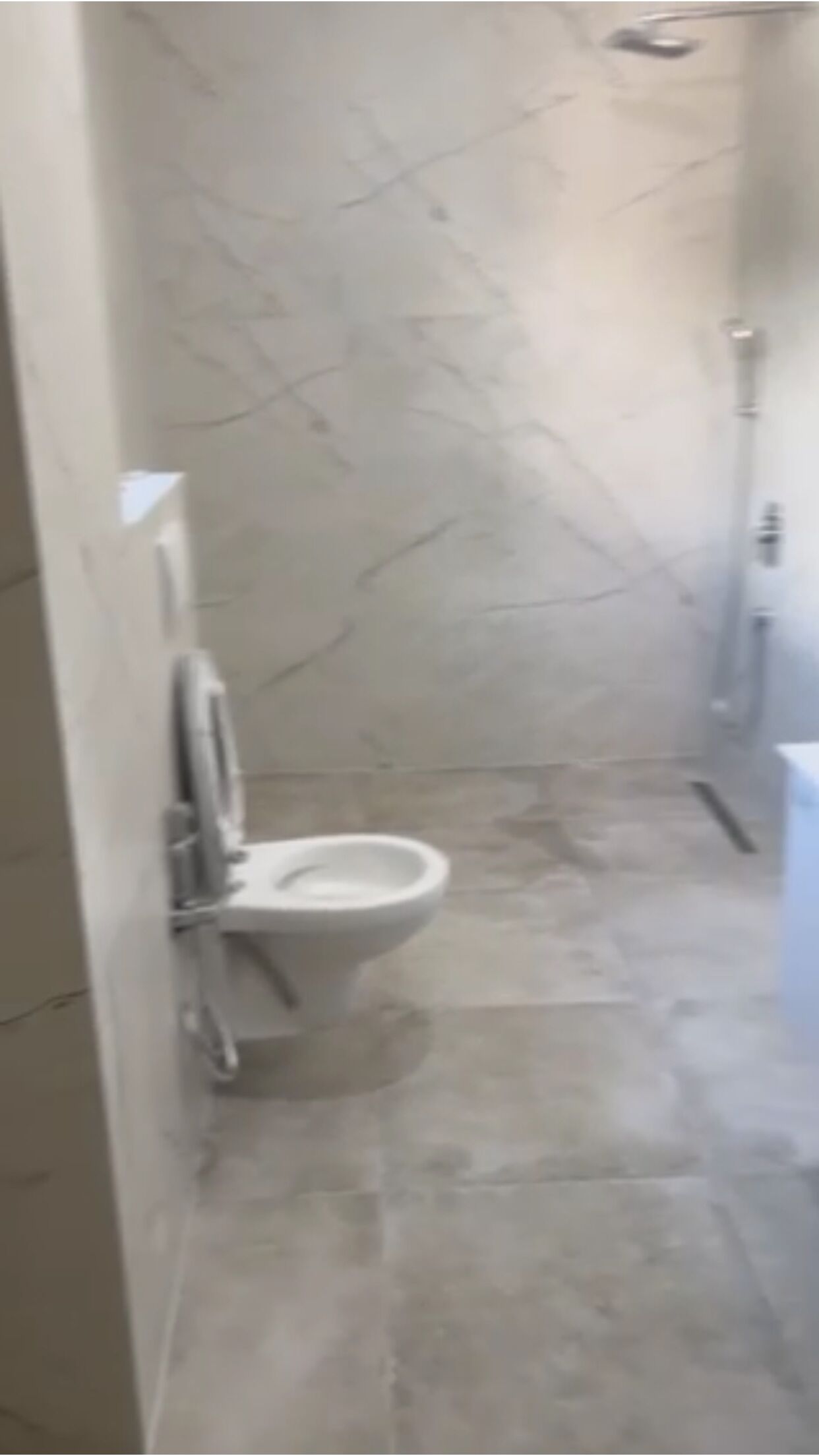 Une salle de bain avec un sol en marbre, des toilettes et un espace douche.