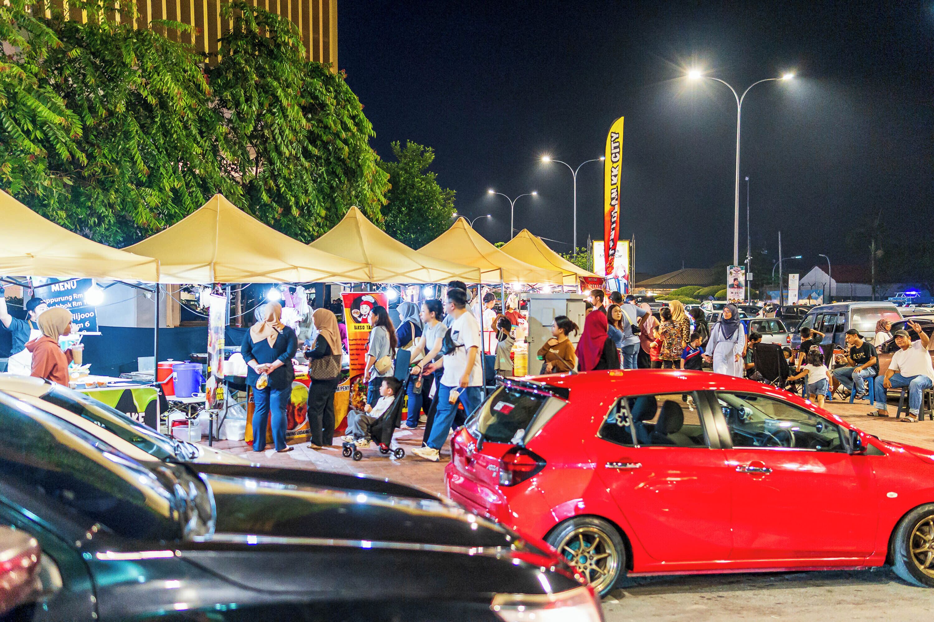 Ein nächtlicher Markt im Freien mit Zelten, Menschen und Autos.