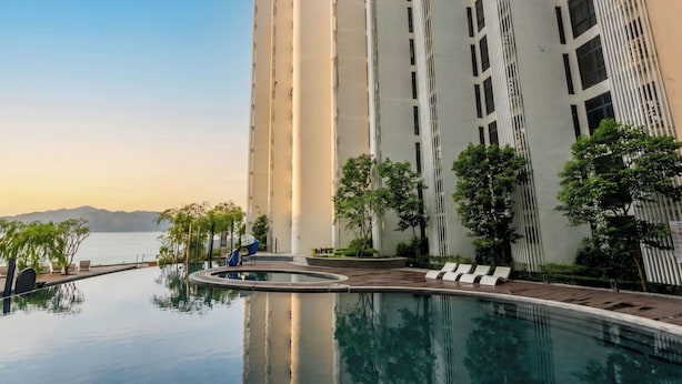 A high-rise building with a reflective pool, lounge chairs, and trees. - The Shore Premier Suites Kota Kinabalu (Kota Kinabalu)
