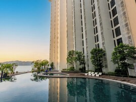 Um edifício alto com piscina refletora, cadeiras de lounge e árvores.