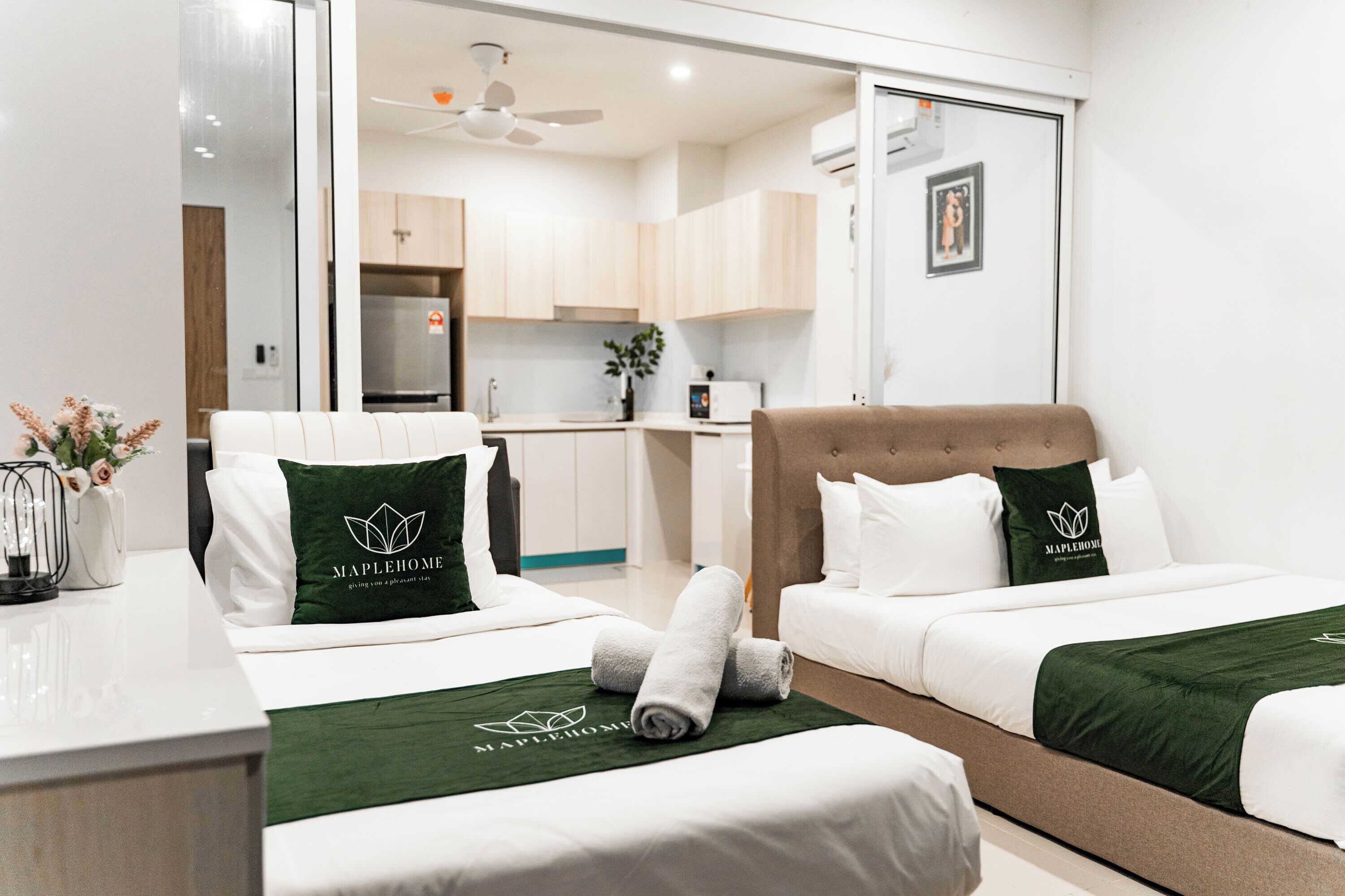 A hotel room with two beds, a desk, a chair, a kitchenette, and a bathroom.