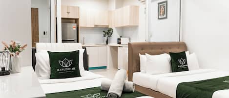 A hotel room with two beds, a desk, a chair, a kitchenette, and a bathroom.