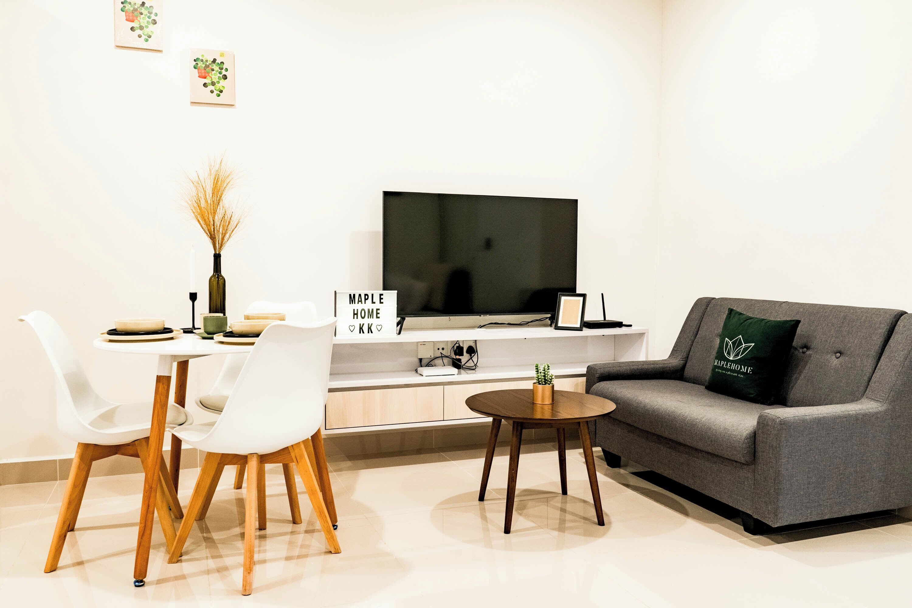 Un salon moderne avec un canapé gris, une table basse, une table à manger avec des chaises, un téléviseur à écran plat et une petite plante en pot.