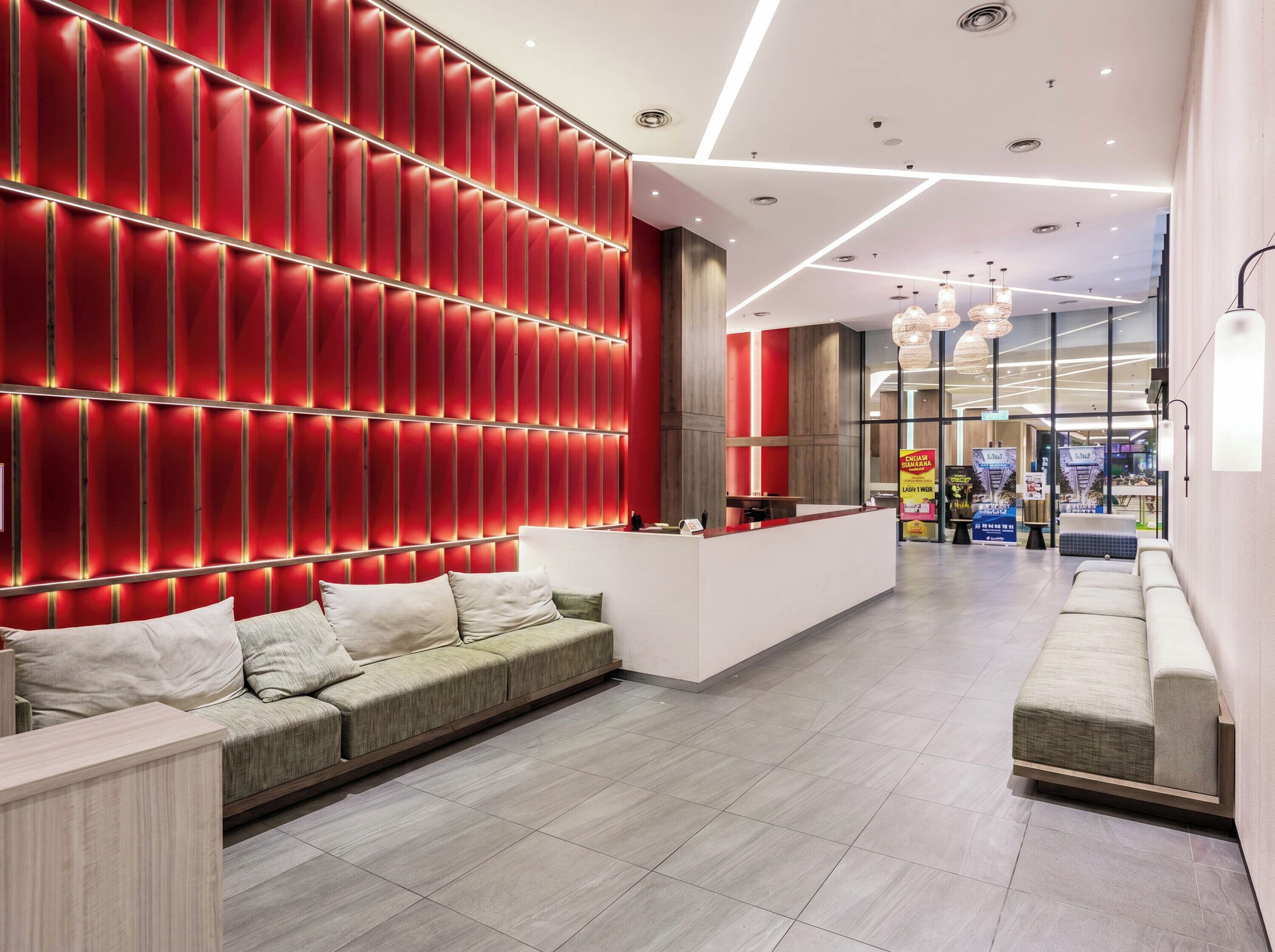 A modern hotel lobby with a red wall, a reception desk, and a seating area.