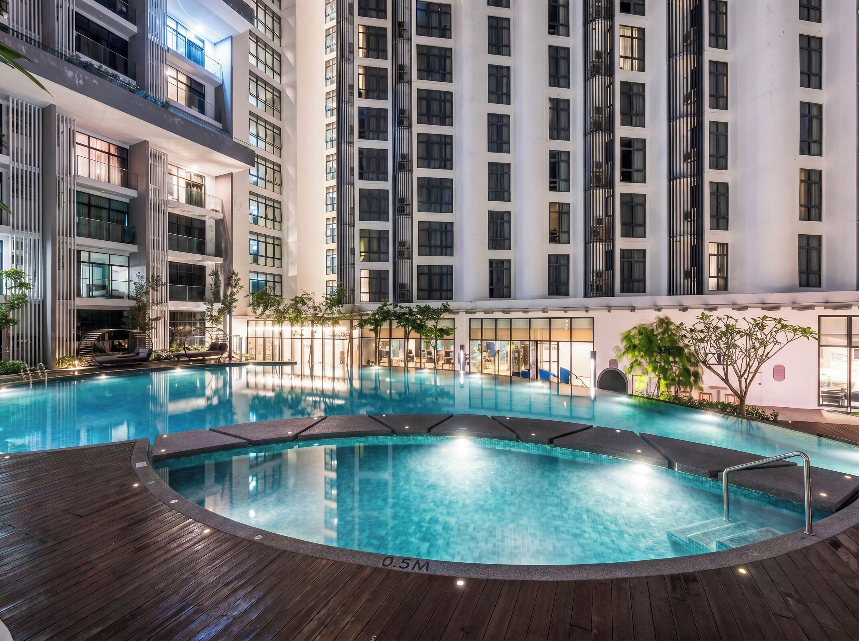 A modern hotel with a large indoor swimming pool, high-rise buildings, and a well-lit outdoor area.