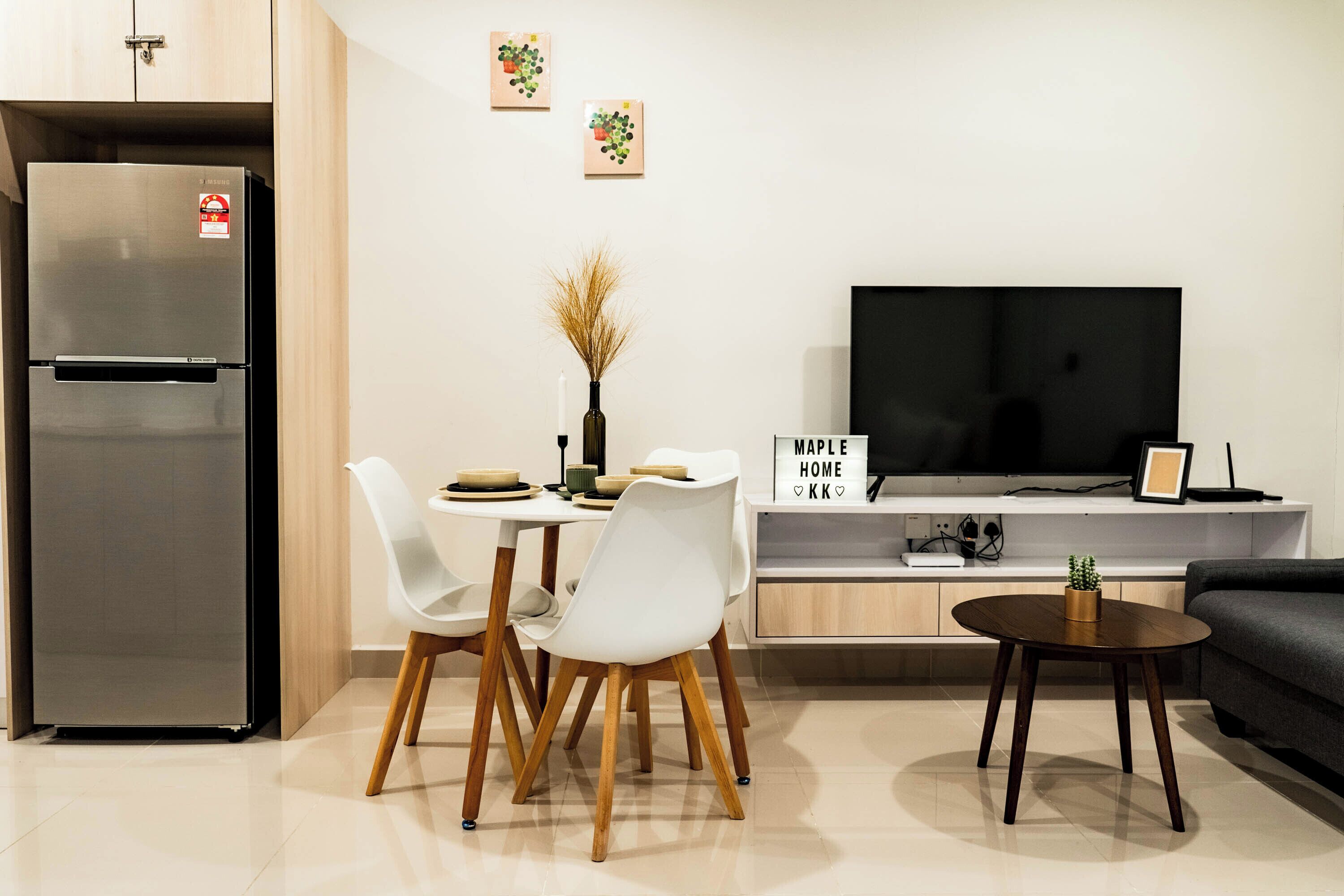 A modern kitchen with a built-in refrigerator, a dining table with chairs, a small side table, a flat-screen TV, and a sofa.
