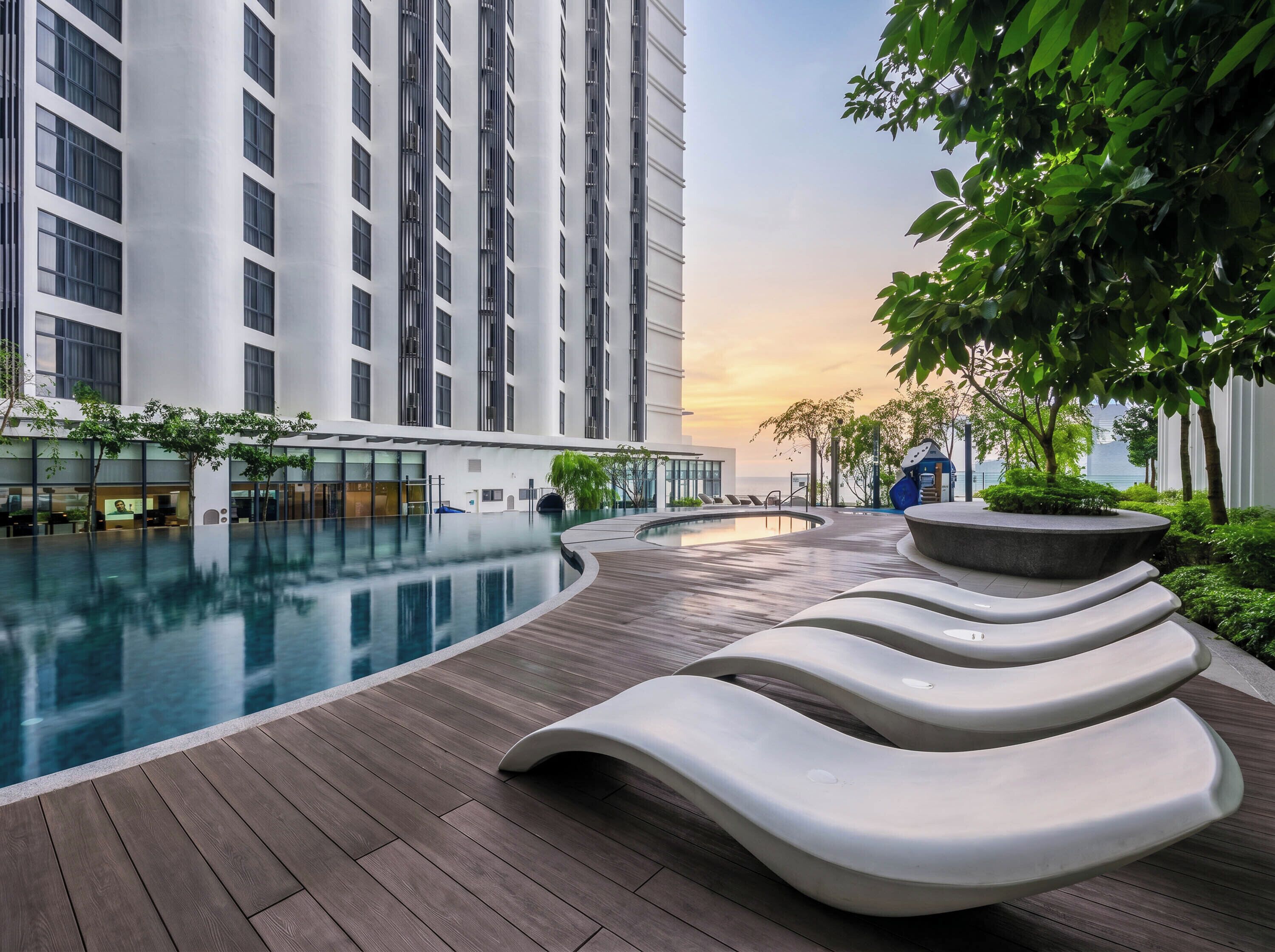 A modern hotel with a swimming pool, lounge chairs, and a view of the sea.