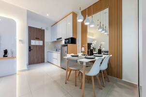 Cozinha moderna com armários brancos, micro-ondas e área de refeições com mesa e cadeiras brancas.