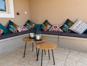 A corner seating area with a stone-tiled floor, a wooden table with two black candle holders, and a variety of patterned cushions. - Casa Plati 1 - Modern Escape with Pool & Garden (Plati)