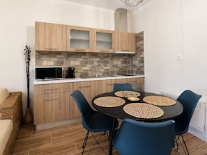 A compact kitchen with wooden cabinets, a microwave, a coffee maker, and a dining table with blue chairs. - Casa Plati 1 - Modern Escape with Pool & Garden (Plati)