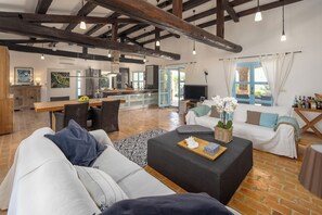 Ein geräumiger Wohnbereich mit Esstisch, Sofas, einem Fernseher und einer Küche im Hintergrund.