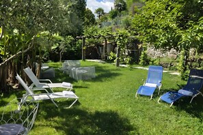 Takapihalla on pergola, kaksi sinistä lepotuolia ja yksi valkoinen tuoli.