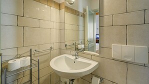 Un baño con un lavamanos blanco, un espejo y una repisa con papel higiénico.
