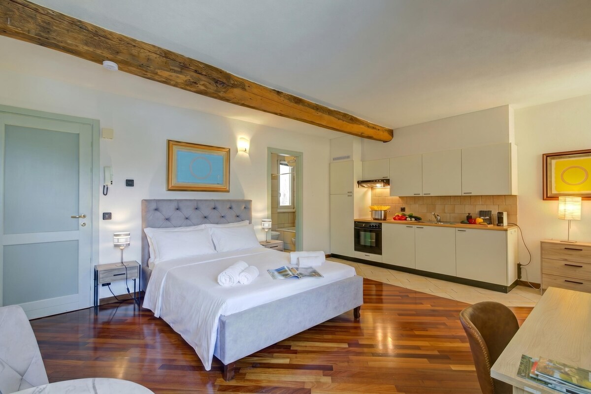 Una camera da letto con un letto grande, un comodino, un tavolino, una trave in legno a soffitto e un angolo cottura, oltre a un tavolo da pranzo.