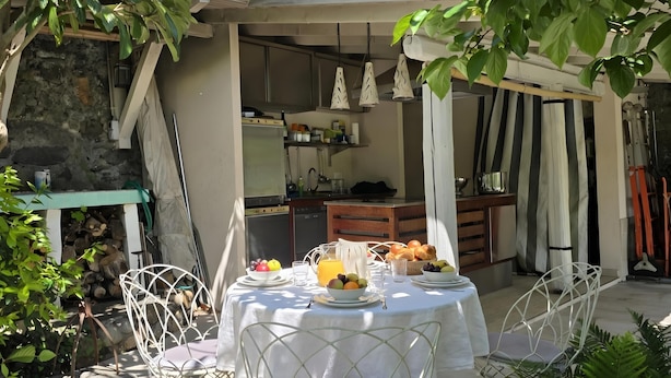Un comedor con una mesa dispuesta para el desayuno, que incluye frutas y una jarra de jugo, con una cocina al fondo.