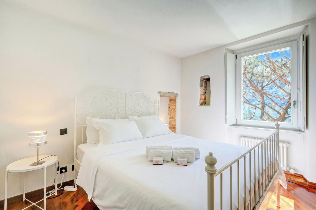 Una camera da letto con un letto, un comodino, una lampada, una finestra e un termosifone.