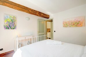 A bedroom with a bed, a white radiator, a wooden ceiling beam, and two paintings on the walls. - Palazzo Gritti Apartments (Morcote)